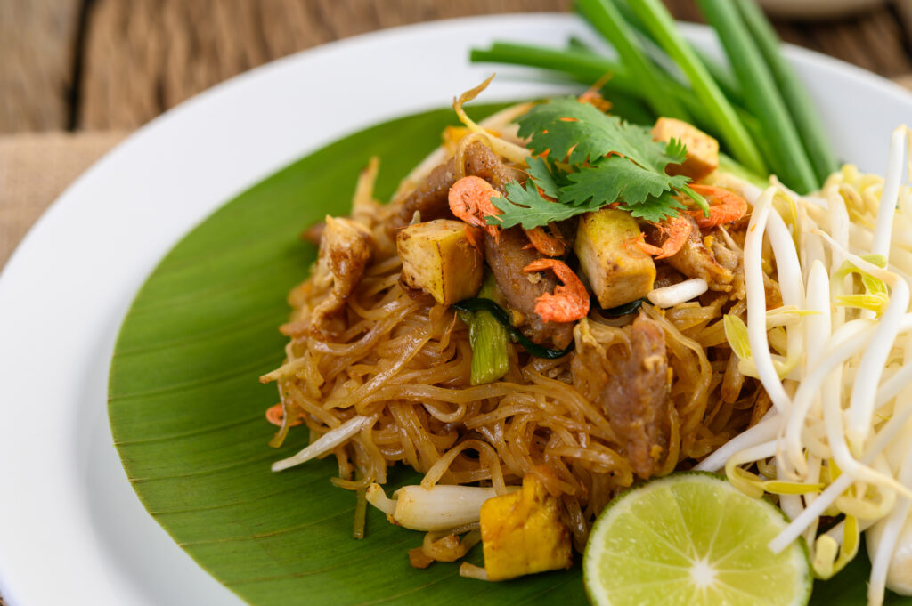 An Authentic Cultural Experience - pad thai in a white plate with lemon on a wooden table